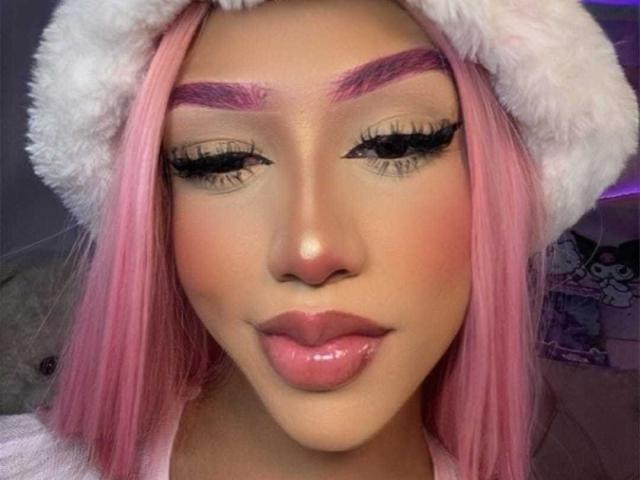 AlissLovely with pink hair, white furry hat, purple eyebrows, long eyelashes, glossy pink lips, and a cute face, looking down with a slight smile.