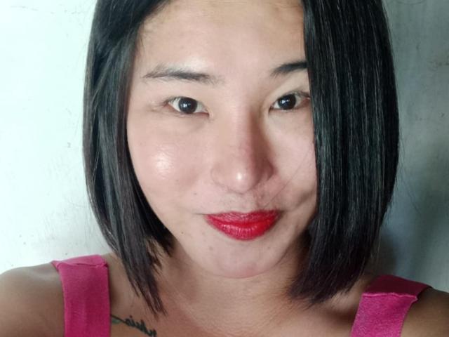 Pinaylaica with short black hair, red lipstick, pink tank top, small tattoo on right side, slight pout, light skin, brown eyes, subtle makeup, soft skin texture.