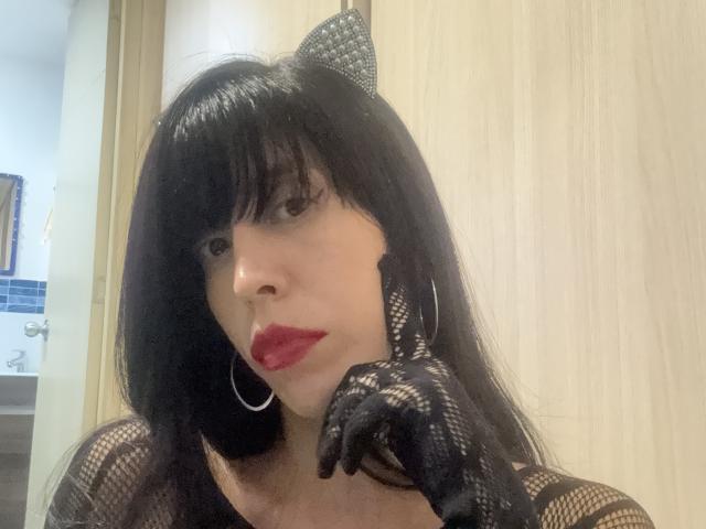 SeleneBrigth with black lace gloves, red lipstick, and hoop earrings, her hand near her face, black hair with a bow, in a photo. Boobs not visible.