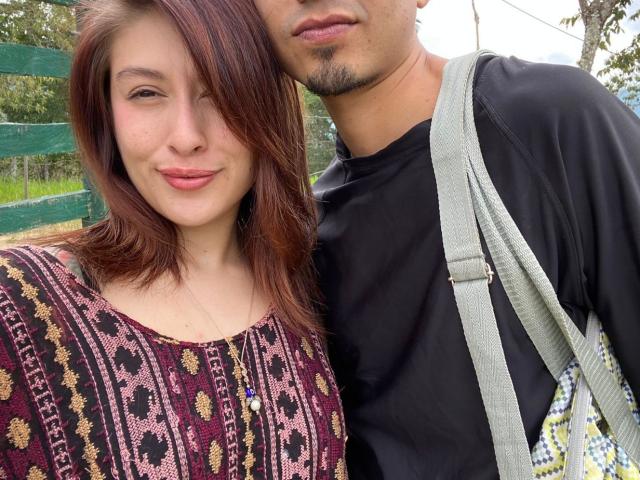 KinkyFarmCouple has a cute, small-ass woman with brown hair in a patterned dress, and a man with a goatee in a black shirt, standing close. He's got a gray strap.