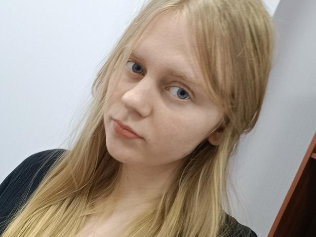 Laliina has pale skin, blue eyes, and long blonde hair, wearing a black top. Her face is slightly tilted with a neutral expression. She has small, slightly upturned tits.