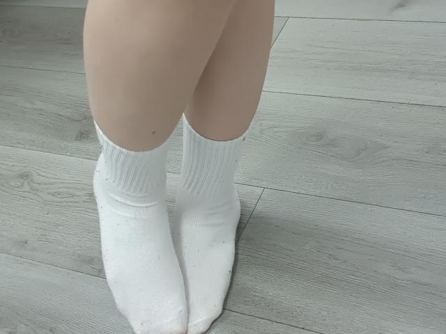 Laliina's pale legs with white socks, standing on grey wooden floor. Socks cover her toes and ankles, showing a bit of skin. No other visible body parts.
