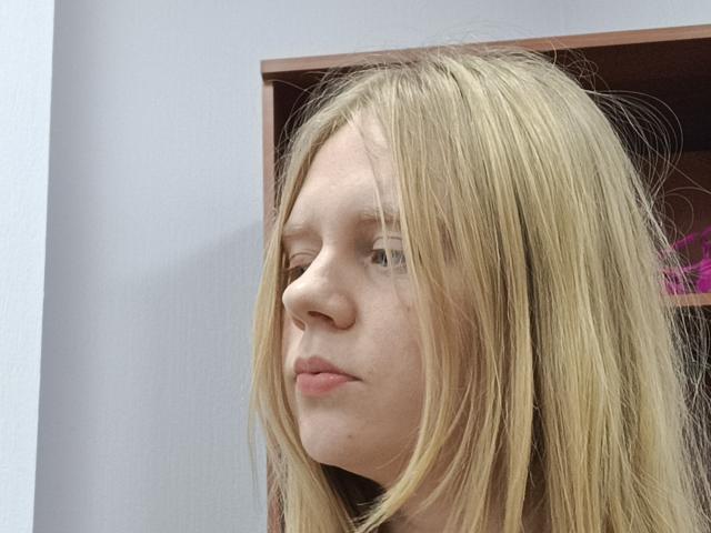Laliina has blonde hair, a pale complexion, and a neutral expression. Her nose is small, and her lips are slightly puckered. Her straight hair falls past her shoulders.