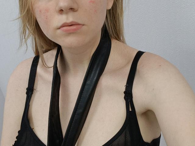 Laliina with light skin, blonde hair, and slight redness on her cheeks, wearing a black mesh bra with straps, showing her small boobs and bare shoulders.