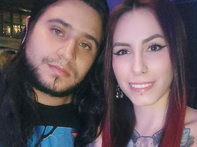 EmilyAndChrisHot have long hair, she's got red highlights, he's got black, she's smiling with a nose ring and lip piercing, he's got a beard and mustache.