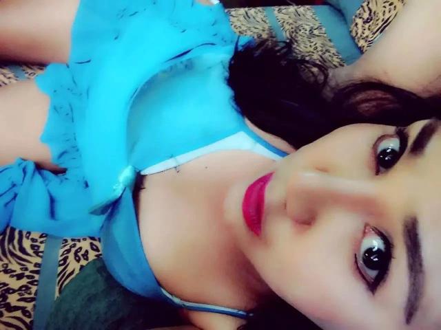 tsLENA4u-mulher atraente com vestido azul, batom vermelho e cabelo castanho ondulado, deitada em uma cama estampada, mostrando o colo e olhando para a câmera com olhos grandes e escuros..