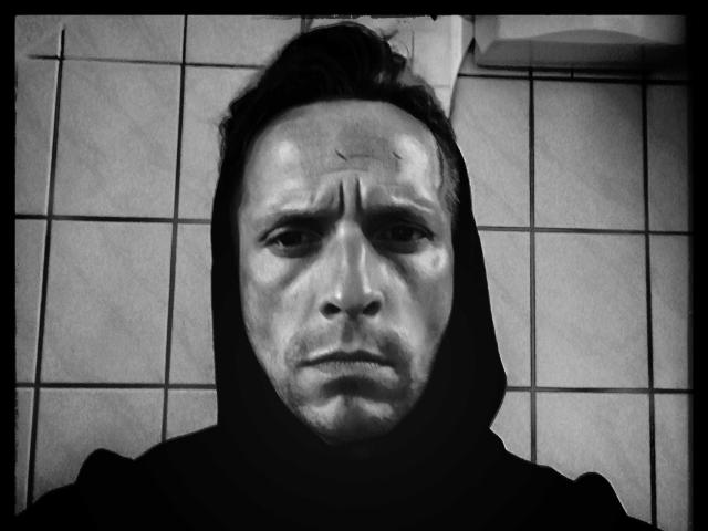 Black and white photo of AgabeyCouple with a serious face, wearing a hood, showing a sweaty forehead and deep-set eyes, with a slightly grumpy expression.