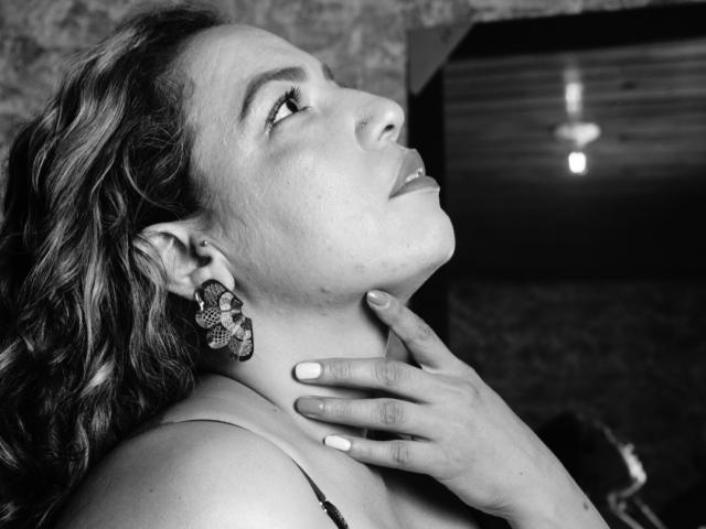 Mariehss with wavy hair, looking up, hand on neck, wearing floral earrings, black-and-white photo, showing her face and hand, slightly parted lips, medium tits, soft light.