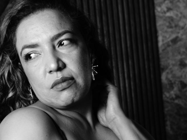 Mariehss has a worried expression, slightly downturned lips, and wavy hair. She's touching her neck with a hand, wearing earrings, in a black-and-white shot.