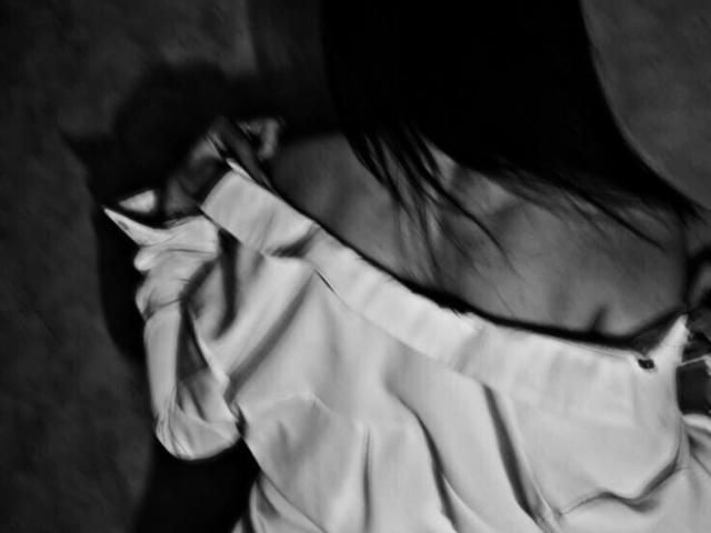 StephanyMays, met haar zwarte haar loshangend, draagt een witte blouse met een open schouder, waarbij haar rechter schouder en een deel van haar bovenrug zichtbaar zijn. Zwart-wit..