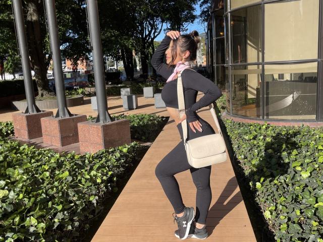 AmaraRicci has black tits, black ass, and black pussy, wearing black leggings and a black long-sleeve top, with a beige bag, standing on a wooden path.