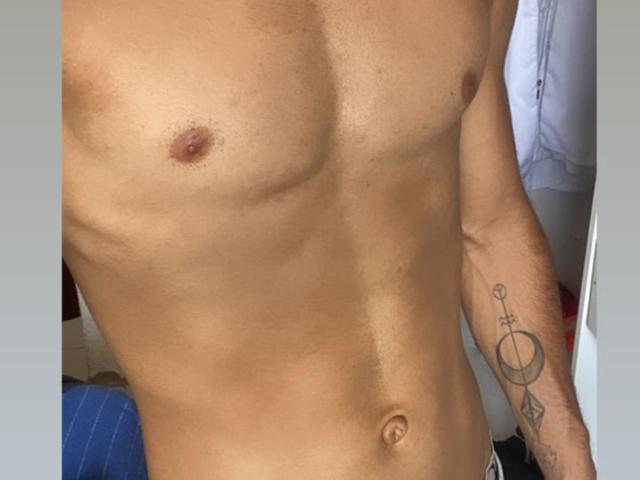 LeonHot69's toned, tan-skinned torso with a small, brown nipple on the left. He has a tattoo of a circle with an 'X' and a diamond on his right arm.