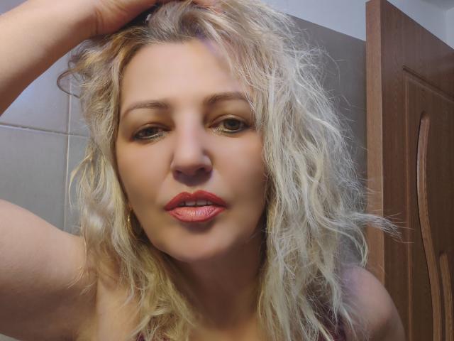 SexyCoco with wavy blonde hair, red lipstick, and a slightly open mouth, touching her head with a hand, showing a cute and sexy face.