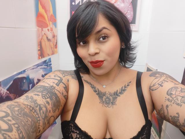 Chili, a tattooed Asian woman with short black hair and red lips, takes a selfie, showing her cleavage in black lace.