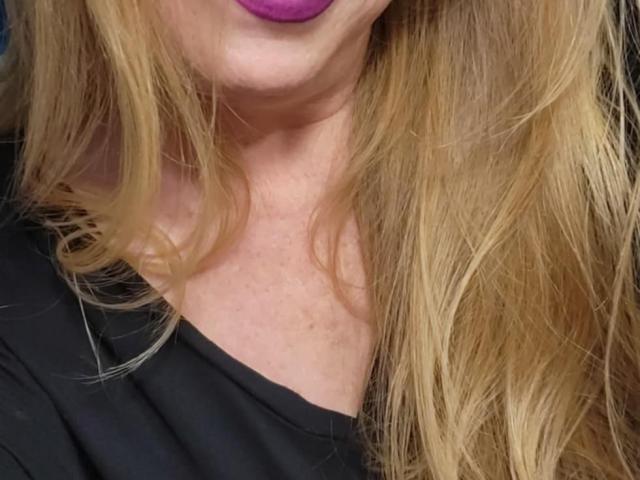 PurplesLips' blonde hair, purple lipstick, black shirt, and fair skin, showing a slight neck and upper chest. Boobs not visible, face mostly out of frame.