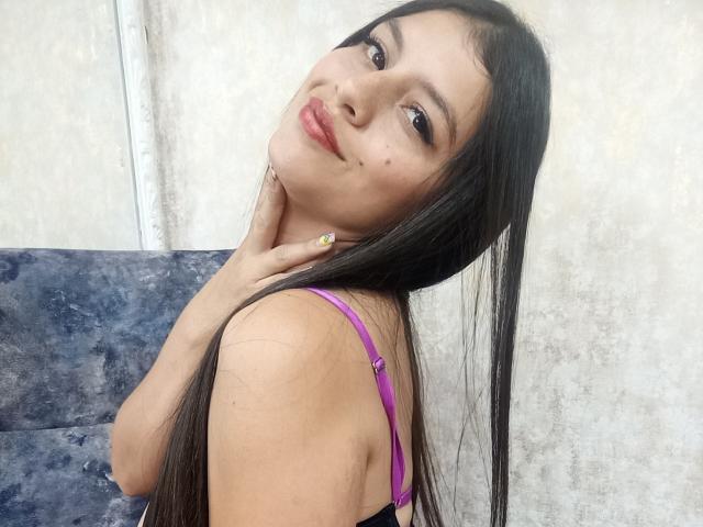 MadissonFontaine with long black hair, purple bra, and yellow nails, tilting head, smiling slightly, hand on neck, smooth light skin, subtle makeup, cute, sexy.