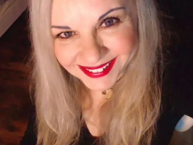 SaraHilton-hot with long blonde hair, red lipstick, and smiling eyes, showing her tits in a black top, wearing a gold necklace, looking up at the camera.