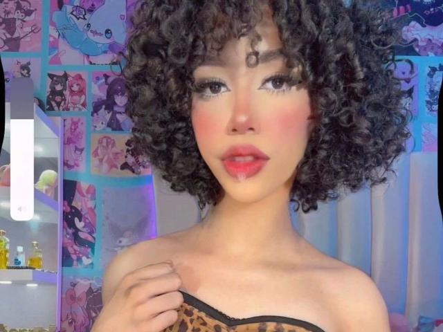 AlissLovely has curly black hair, pink blush, red lipstick, and is wearing a strapless leopard print top. Her hand is on her shoulder, showing off her tits.