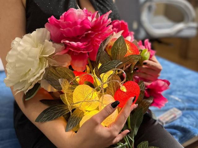 Janel's hands holding a colorful bouquet with pink, white, and yellow flowers, and glittery red and yellow hearts. Her black nails are visible.