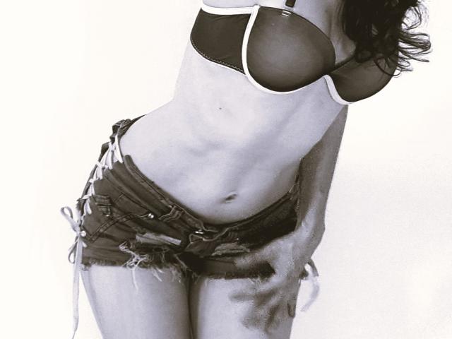 HarlyMia's tits in a black bra, wearing frayed denim shorts with white lace-up sides, leaning forward, showing a slim, toned belly and a hint of her ass.