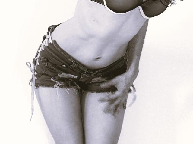 HarlyMia with small tits in a black bra, wearing frayed, lace-up denim shorts, standing with a slightly bent-over posture, hand on thigh, monochrome, slightly textured.