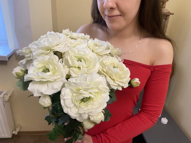 JoannaSia with off-shoulder red dress, holding white rose bouquet, has small tits, brown hair, smiling, wearing silver necklace, in a room with white window.