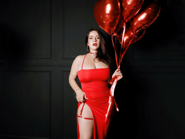 ChristineBray with big boobs in a red dress holding shiny red balloons, standing against a dark wall, looking confident, long brown hair, red lipstick, sexy, elegant.