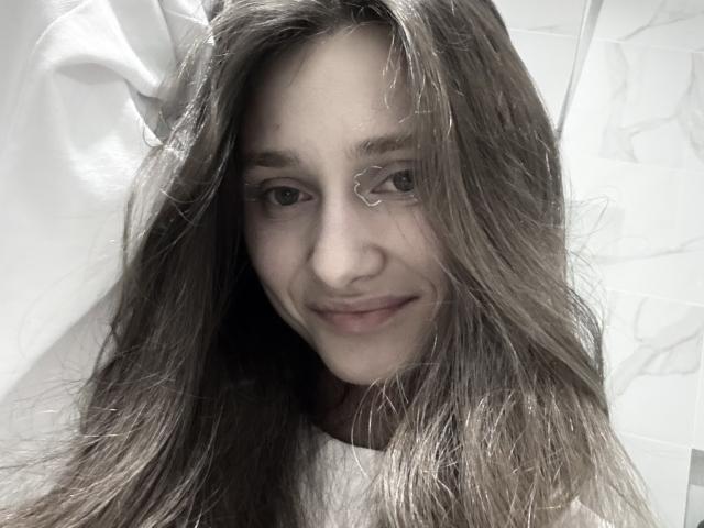 LaraSweetyHot, avec ses longs cheveux bruns, son léger sourire et son visage mignon, regarde l'appareil photo. Son nez est petit et elle porte un maquillage discret. Ses seins ne sont pas visibles..