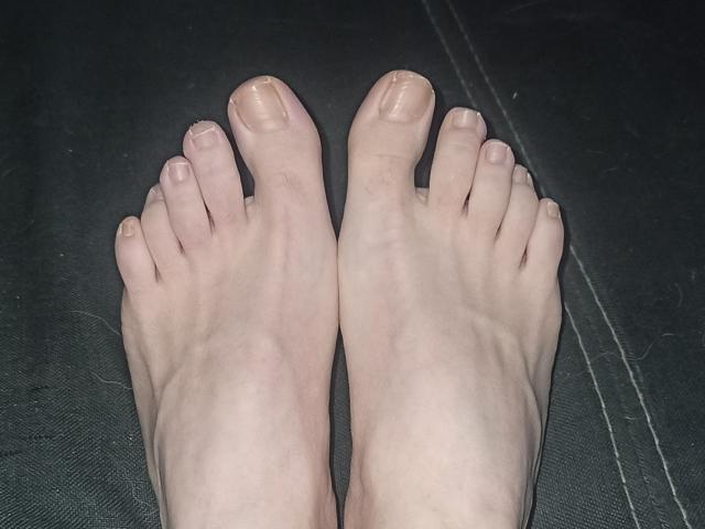 LolaGlamlolaChaude's pale feet with slightly dirty toes, lying flat on a dark surface. Her toes are spread apart, showing the bottoms of her feet clearly.