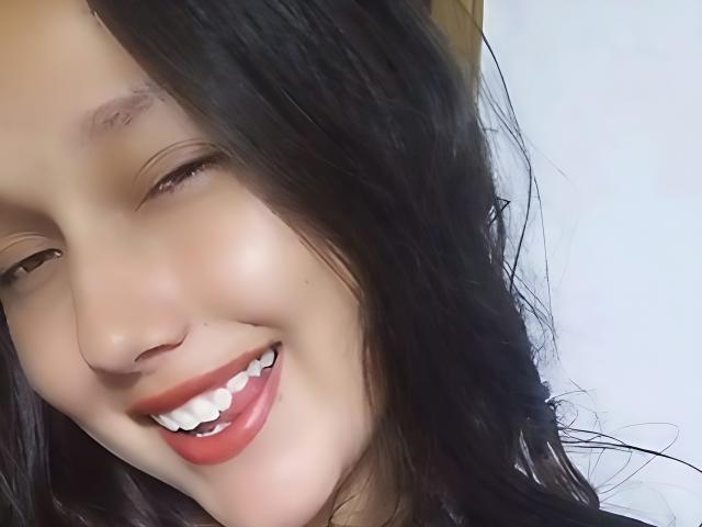 JenniferLw's smiling face with dark, wavy hair, red lipstick, and white teeth. She's looking sideways with a cute, playful expression. Her nose is slightly upturned.