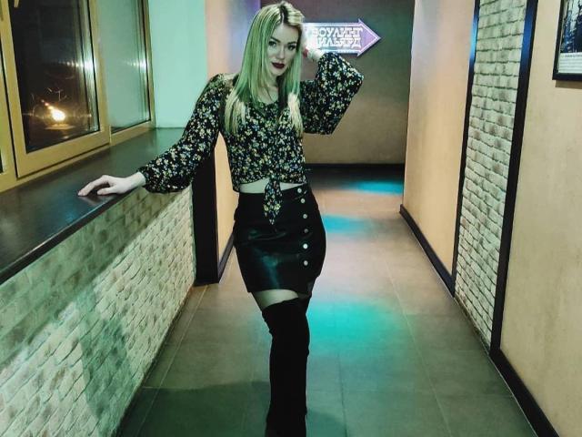 BrightBliss has blonde hair, floral blouse, black leather skirt with buttons, thigh-high boots, and a white belt, standing in a neon-lit hallway, looking confident with a hand on her hip.