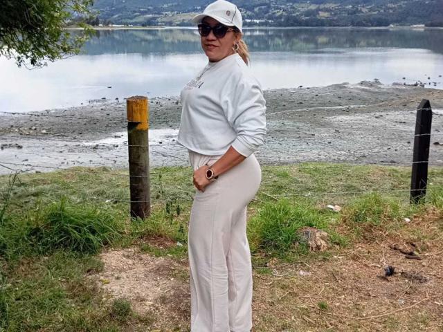 JadeSexiest with blonde ponytail, white cap, black sunglasses, white sweatshirt, and white pants, stands by a wire fence, hands in pockets, showing her round ass.