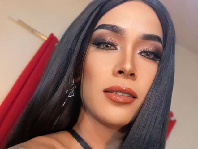 SexyHotAmara with long black hair, brown eyes, thick eyebrows, orange lipstick, and shiny eyelids, wearing star earrings, looking directly at the camera with a slightly open mouth.