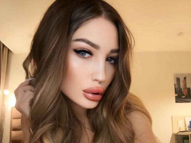 Martinik tiene labios carnosos, ojos azules y cabello largo y castaño, mirando a la cámara con un ligero puchero. Su maquillaje incluye delineador de ojos grueso y un brillo de labios rosa..