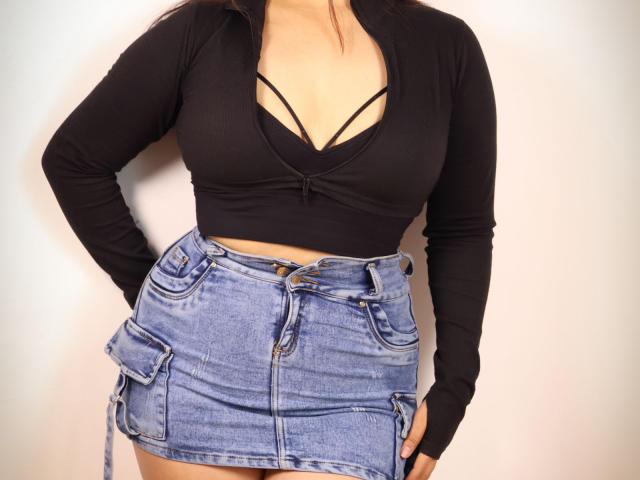 AshleyWalkerI has big tits, wearing a black long-sleeve crop top with a deep V-neck, and a blue denim skirt with side pockets and buttons.