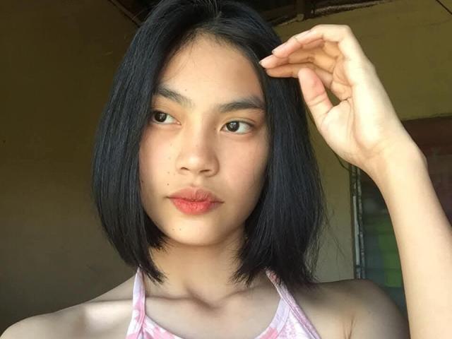 XAkariMorisX has black shoulder-length hair, light skin, brown eyes, and pink lips. She's wearing a pink checkered halter top, with her right hand touching her hair.