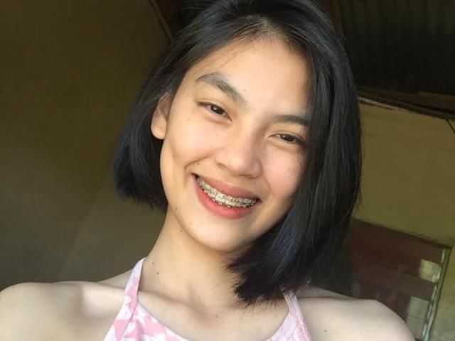 XAkariMorisX with a cute smile, showing metal braces, short black hair, and a pink patterned halter top, in a bright, sunny selfie.
