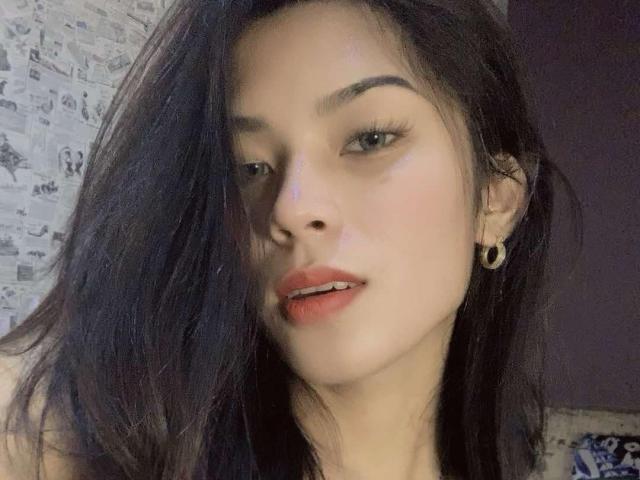 XHellyMariaX has dark hair, green eyes, and red lips with slightly parted teeth. She's wearing small ear gauges and looking at the camera with a relaxed expression.