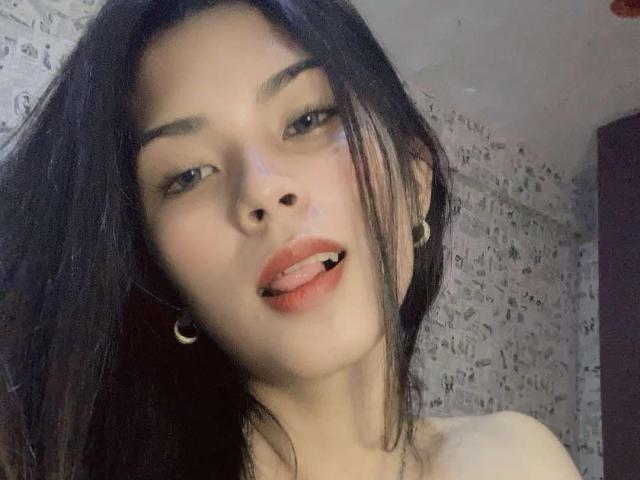XHellyMariaX with black hair, light skin, and small hoop earrings, sticking out her tongue with red lips, wearing a strapless top, looking at the camera.