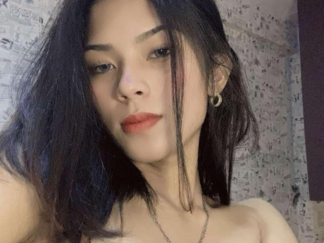 XHellyMariaX heeft donker, rommelig haar, een lichte huid en rode lippenstift. Ze draagt een maanvormige oorbellen en een ketting, met een serieuze, licht verleidelijke uitdrukking..