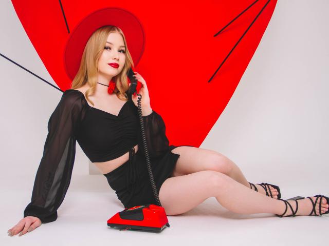 NicoleBrian con un teléfono rojo, una blusa transparente negra, pantalones cortos, un sombrero rojo, sosteniendo el teléfono, sentada, con las piernas cruzadas, tacones negros con tiras, piel clara, cabello rubio, lápiz labial rojo, segura de sí misma, sexy..