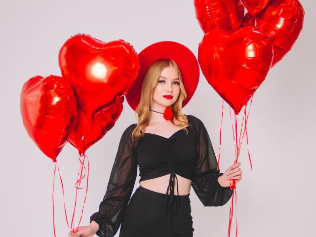 NicoleBrian with red heart balloons, wearing black sheer top, black skirt, red hat, red lipstick, holding balloons, her ass slightly visible, blonde hair, white background.