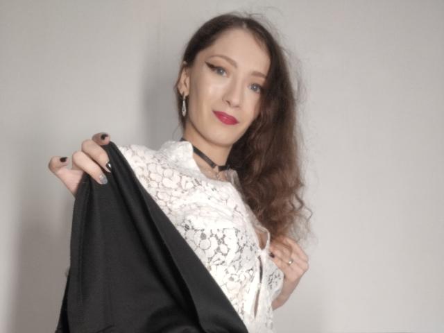 Silerta tiene el pelo largo y castaño, una blusa blanca de encaje, un collar negro y una chaqueta negra, mostrando sus pechos con una sonrisa segura y lápiz labial rojo. Está mirando a la cámara..