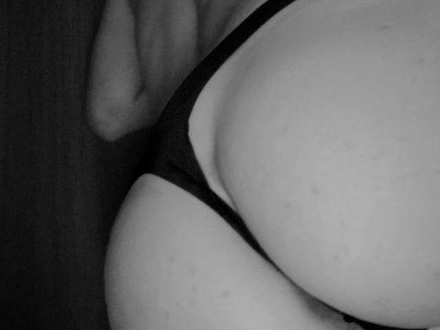 HazelR's ass in black thong, showing a curved, pale, slightly freckled buttock, with a visible hand resting on the left side. Black-and-white, close-up, intimate shot.