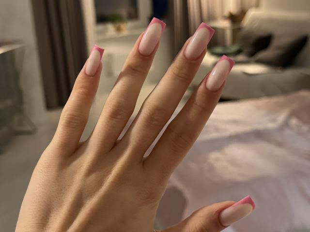 La main de LaraSweetyHot, avec des ongles manucurés à la française en rose et blanc, mettant en valeur ses ongles soigneusement coupés, brillants et avec des pointes roses. Ses doigts sont légèrement écartés..