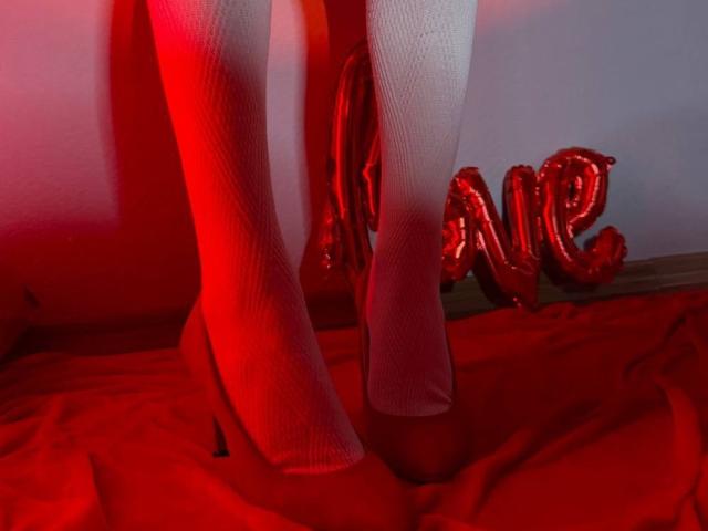 Lialit's white knitted socks and red high heels on a red cloth, with a red "NE" balloon in the background, illuminated by red and pink lighting.