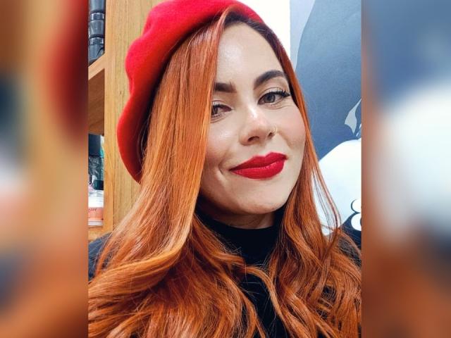 DulceCharlotteHot with red hair, red beret, and red lipstick, smiling at the camera, wearing a black turtleneck. Her tits are not visible. Her nose is pierced.
