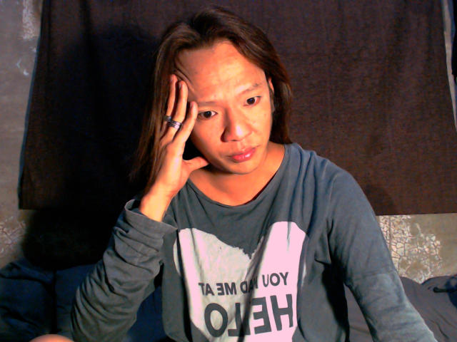 NaughtySexFrYou has medium-length brown hair, a slightly worried expression, and wears a blue shirt. She's touching her head with her left hand, showing a ring on her finger.