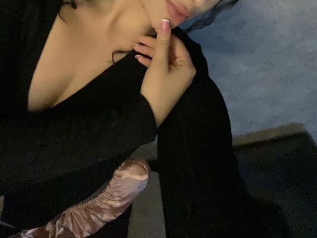 I seni di Olieri sono scoperti sotto una maglietta nera, mentre nella sua mano destra, con le unghie rosa, tiene un pene eretto, rosa e venato. Ha un leggero sorriso..