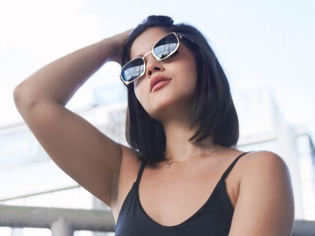 ScarlletZhen com cabelo curto preto, vestindo uma regata preta, óculos de sol e um colar, com a mão no cabelo, olhando para cima, luz suave, sorriso discreto, confiante, sexy, fofa..
